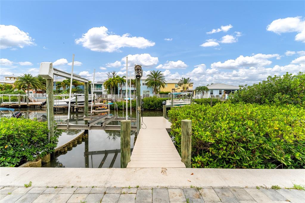 A wooden dock leads to a boat lift on a canal surrounded by lush greenery — 6412 KEY ISLAND AVENUE, APOLLO BEACH, FL