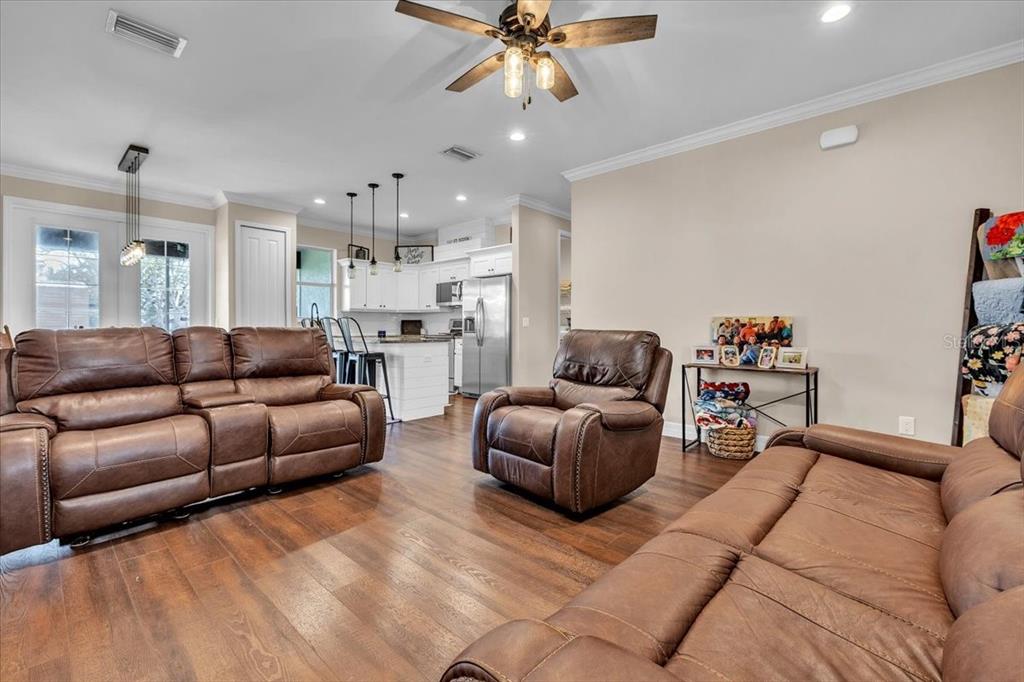 A living room with brown leather furniture, wood-look flooring, and an open kitchen in back — 8429 SW RIVERVIEW OAKS TERRACE, ARCADIA, FL