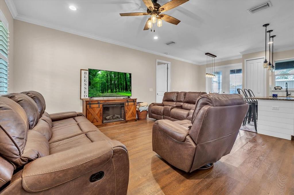 A living room features brown leather furniture, a fireplace console, and wood-look flooring — 8429 SW RIVERVIEW OAKS TERRACE, ARCADIA, FL