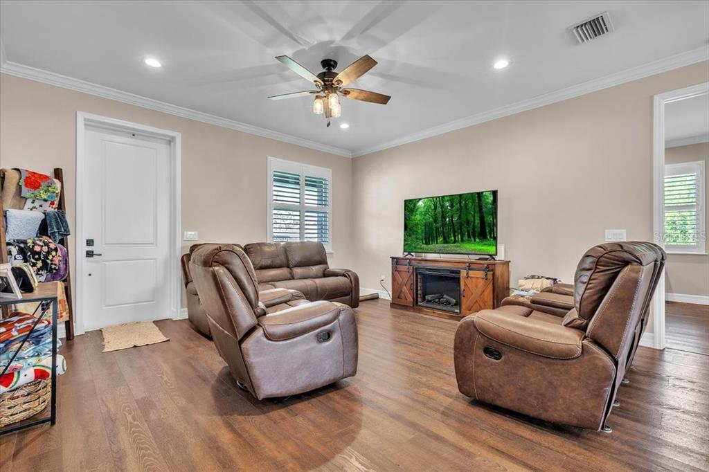 A living room features brown leather reclining furniture, a television on a wooden stand, and hardwood floors — 8429 SW RIVERVIEW OAKS TERRACE, ARCADIA, FL