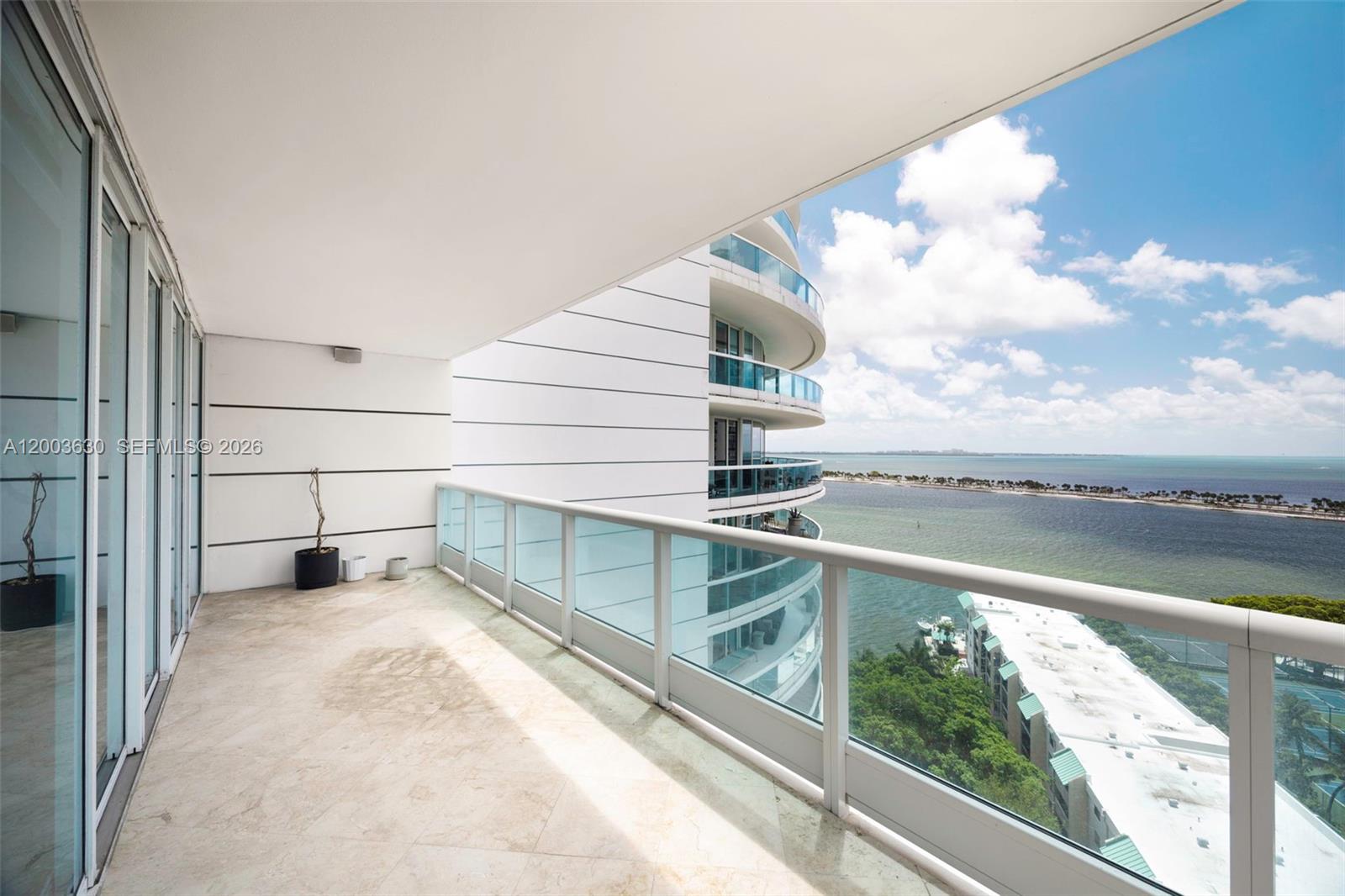 A spacious balcony with stone flooring and glass railings overlooks the ocean and nearby buildings — 2127 Brickell Ave # 1805, Miami FL 33129, MIAMI, FL
