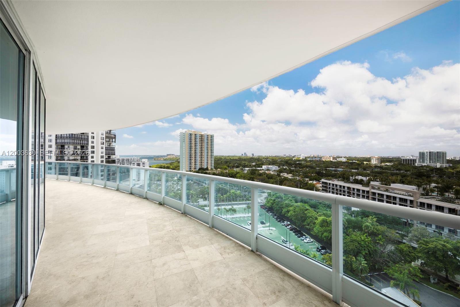 A wide, curved balcony with tile flooring overlooks a city landscape and green trees — 2127 Brickell Ave # 1805, Miami FL 33129, MIAMI, FL