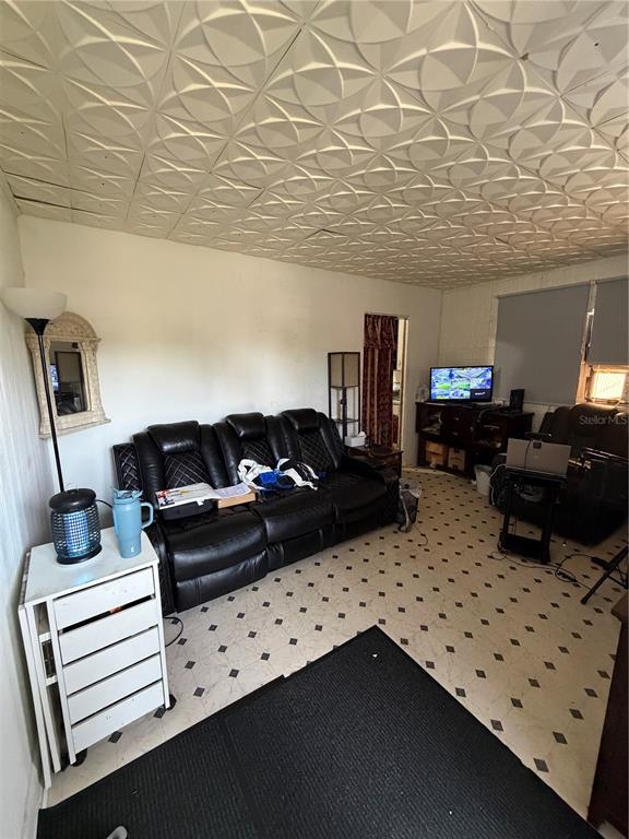 A living room features a black leather sofa, patterned ceiling tiles, and light-colored vinyl flooring — 6923 ANOKA DRIVE, ORLANDO, FL