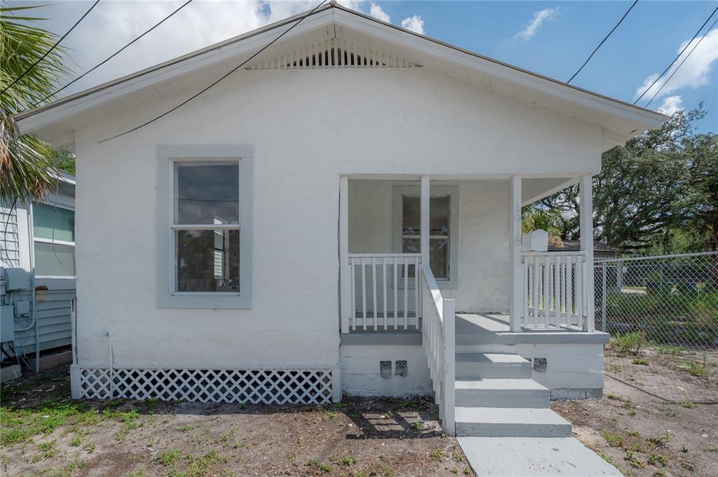 A small, white, single-story house with a front porch, stairs, and a chain-link fence — 1918 E 21ST AVENUE, TAMPA, FL