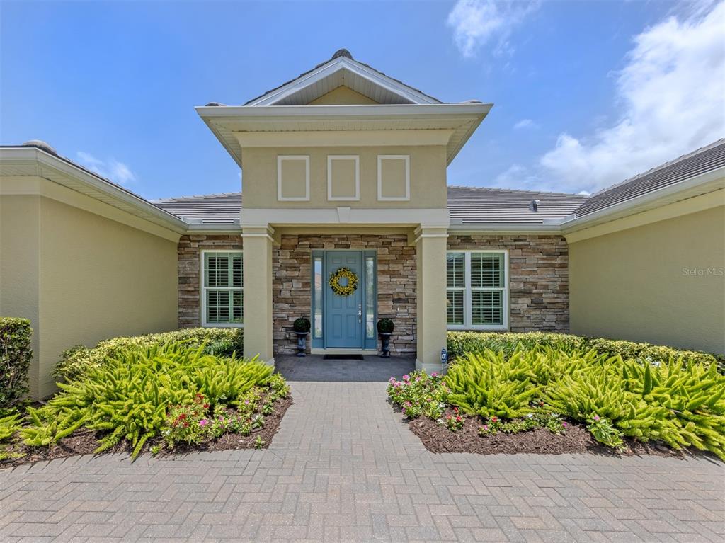 The exterior of a house features a stone facade, a blue front door, and landscaping — 19751 COBBLESTONE CIRCLE, VENICE, FL