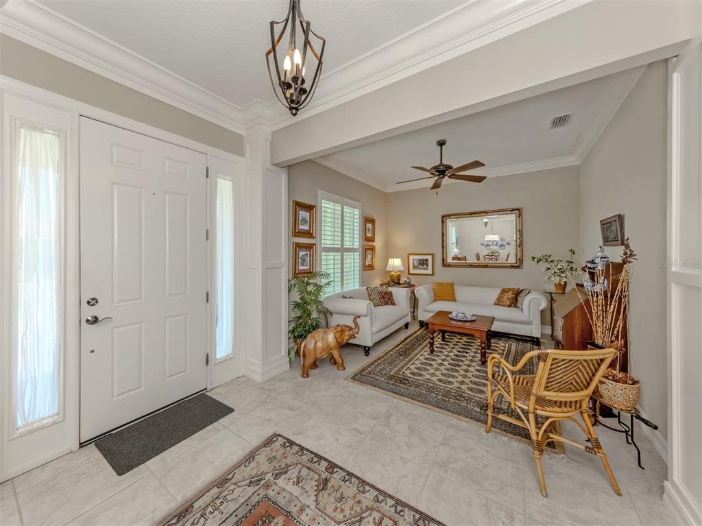 A bright entryway with tile floors leads into a living room with white sofas — 19751 COBBLESTONE CIRCLE, VENICE, FL