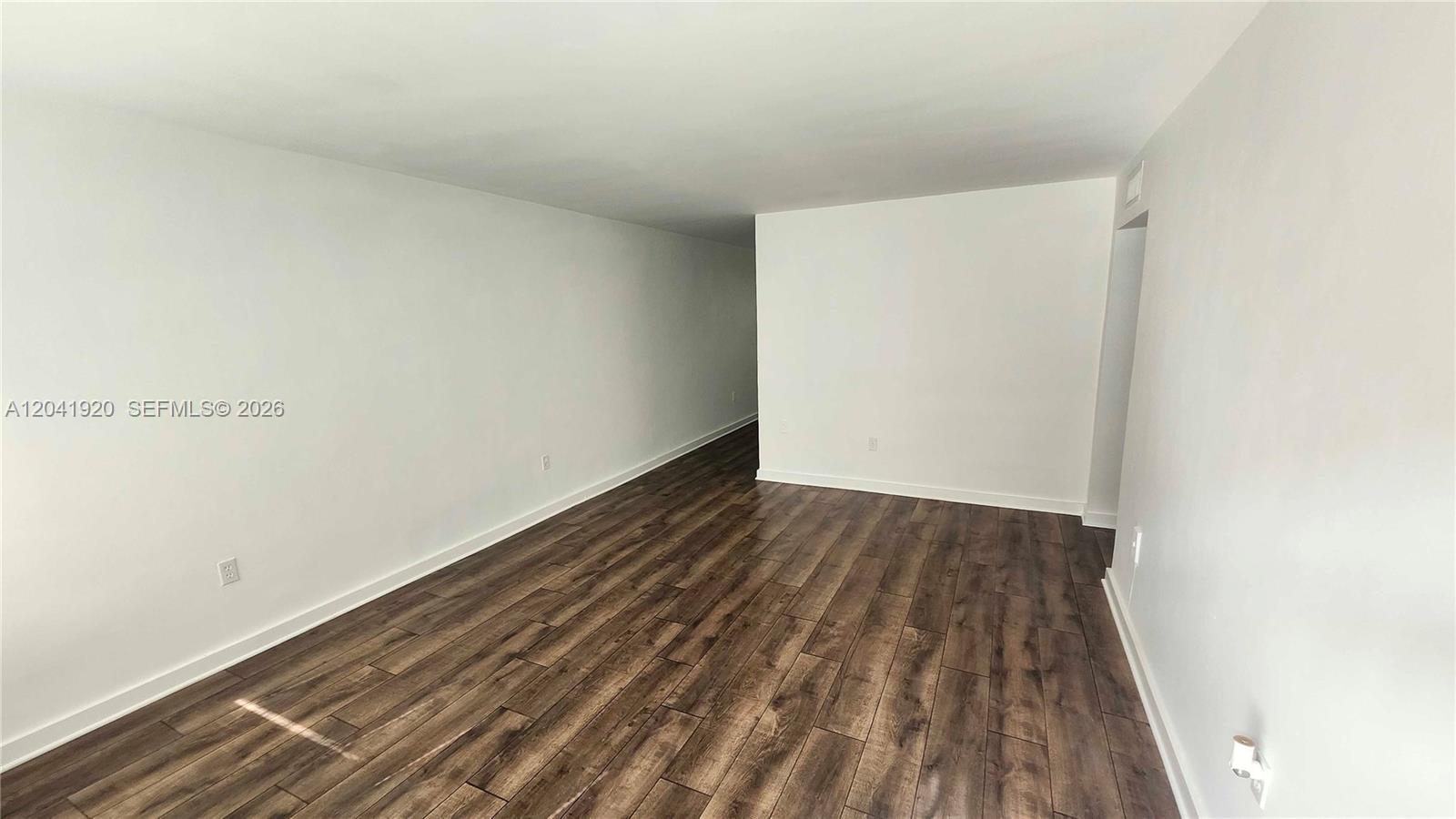 An empty room features white walls and dark wood-look laminate flooring — 111 NW 152nd St # 11, Miami FL 33169, MIAMI, FL
