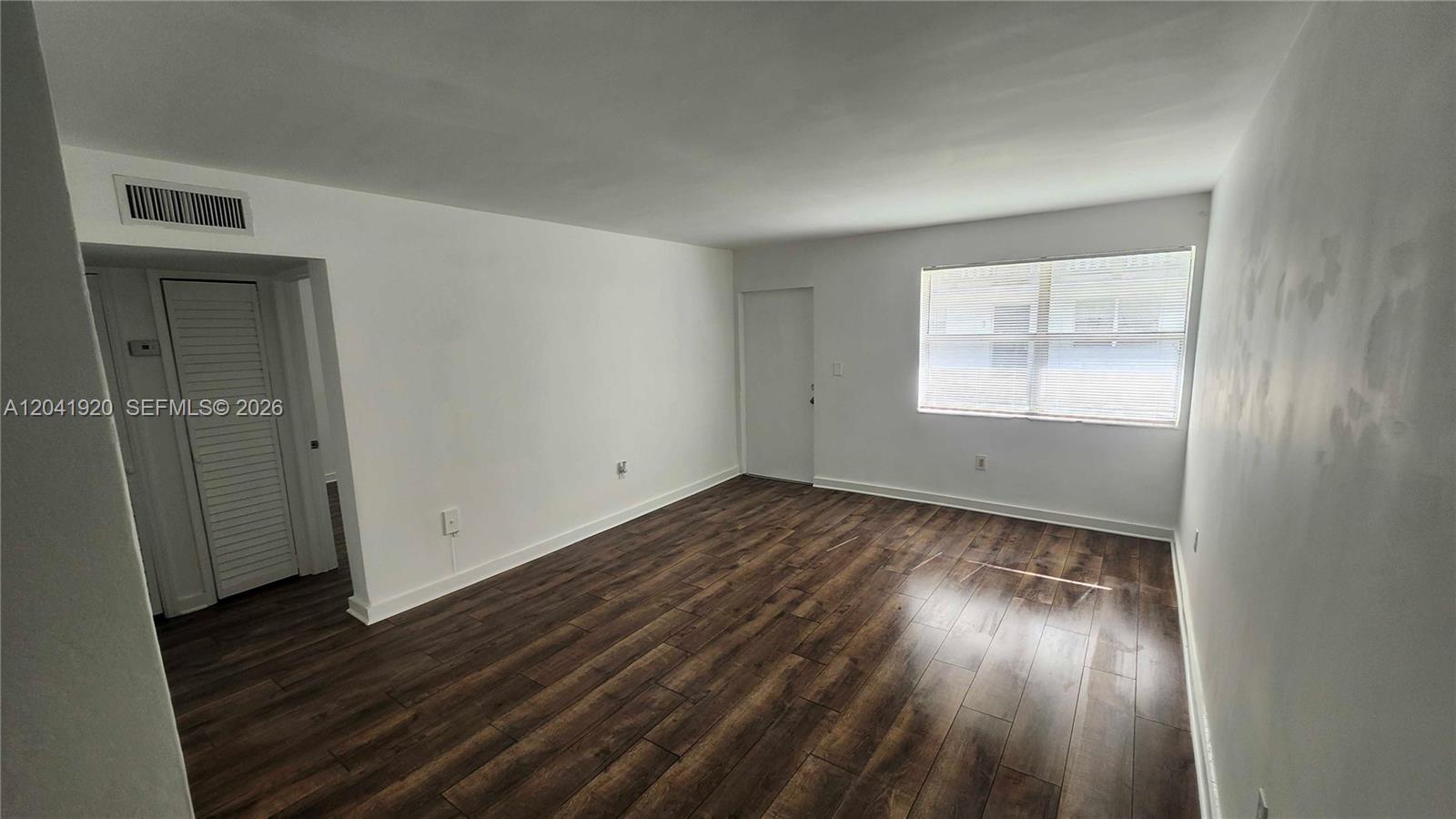 An empty room features white walls, dark wood-look flooring, and a single window with blinds — 111 NW 152nd St # 11, Miami FL 33169, MIAMI, FL