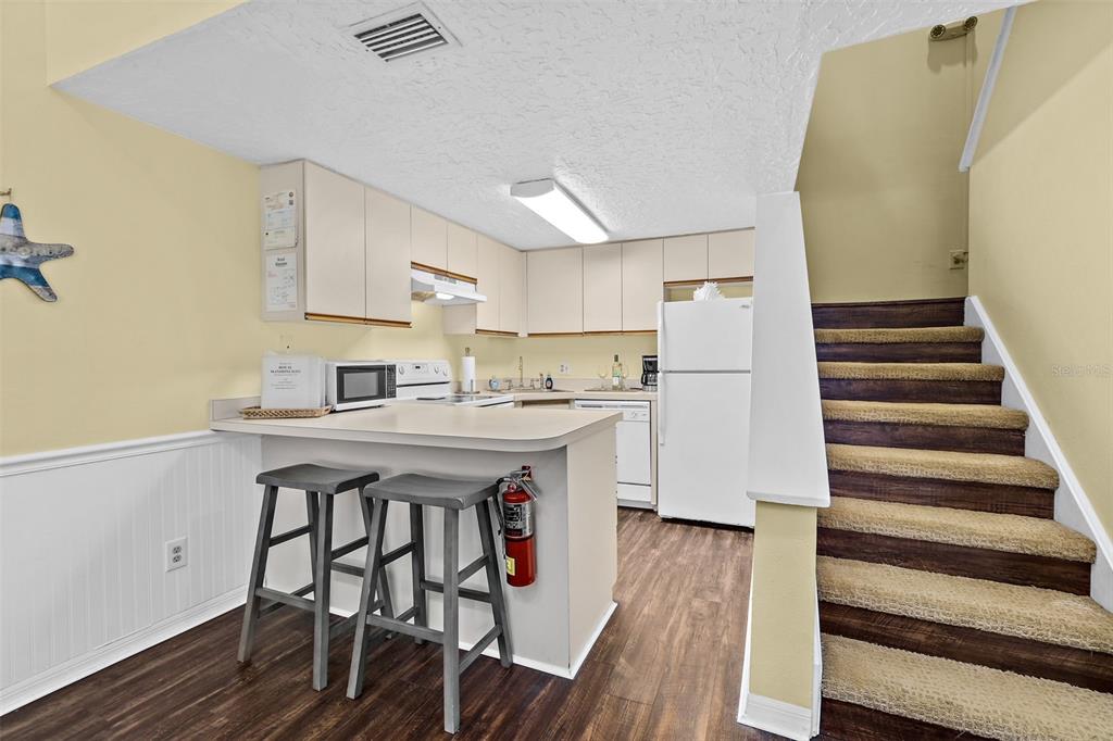 A kitchen with white cabinets, a breakfast bar with two stools, and carpeted stairs — 8600 RIDGEWOOD AVENUE UNIT 1311, CAPE CANAVERAL, FL