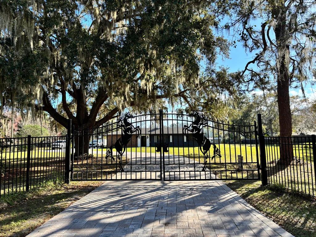 A black metal gate featuring horse silhouettes stands at the entrance of a paved driveway — 1800 GRANADA BOULEVARD, KISSIMMEE, FL