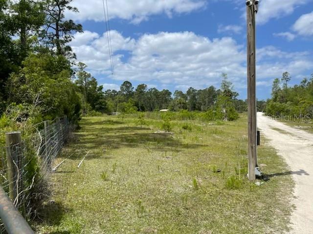 A dirt road runs alongside a grassy, undeveloped lot bordered by a wire fence — 8107 W MAYFAIR DRIVE, HOMOSASSA, FL