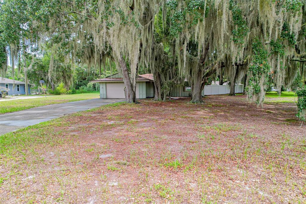A house with a two-car garage sits behind large trees draped in Spanish moss — 4604 CRYSTAL BEACH ROAD, WINTER HAVEN, FL
