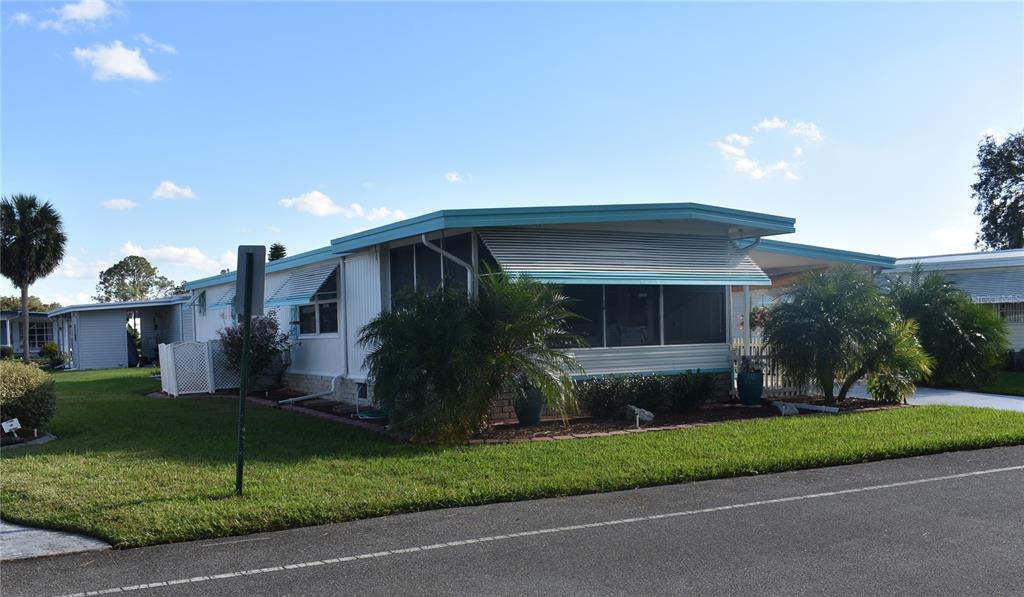 A single-story manufactured home with a screened-in porch and a carport under a blue roof — 410 HAWTHORNE BOULEVARD, LEESBURG, FL