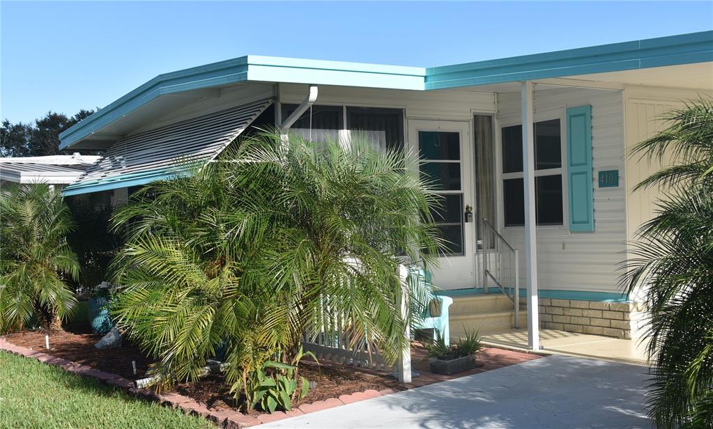 A mobile home exterior features a teal roofline, white siding, a palm tree, and stairs — 410 HAWTHORNE BOULEVARD, LEESBURG, FL