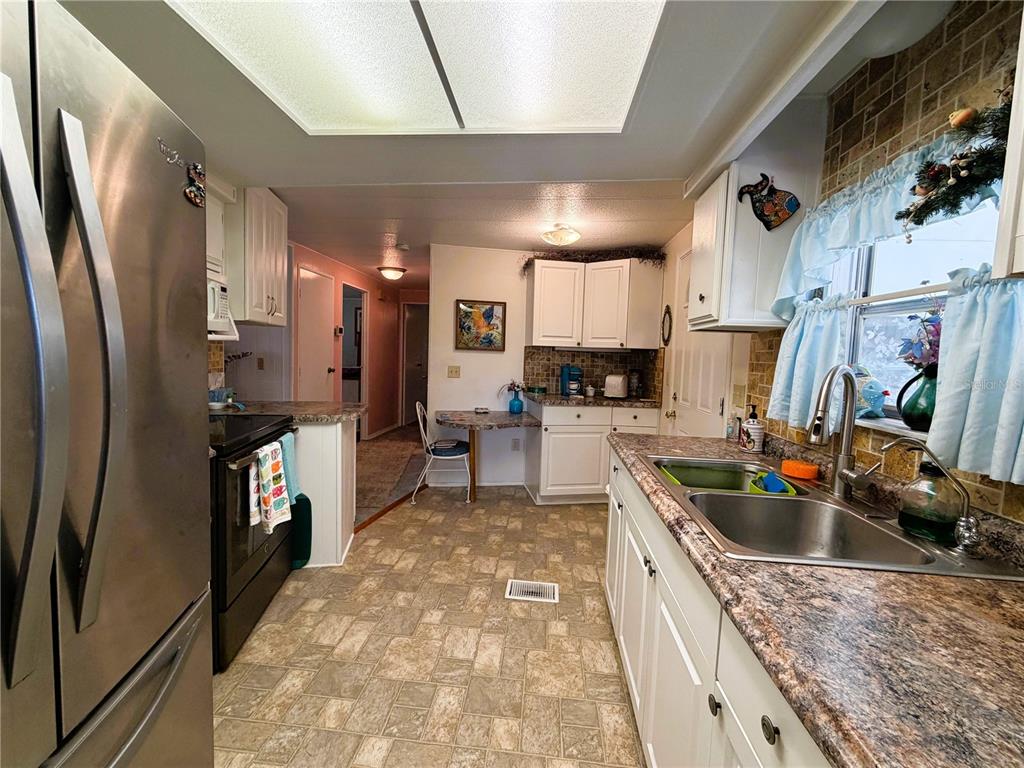 A kitchen with white cabinets, granite-look countertops, stainless steel appliances, and a small dining nook — 410 HAWTHORNE BOULEVARD, LEESBURG, FL