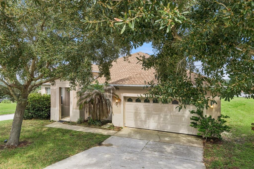 A tan single-story house with a two-car garage and a large tree in the front yard — 780 LAKEVIEW POINTE DRIVE, CLERMONT, FL
