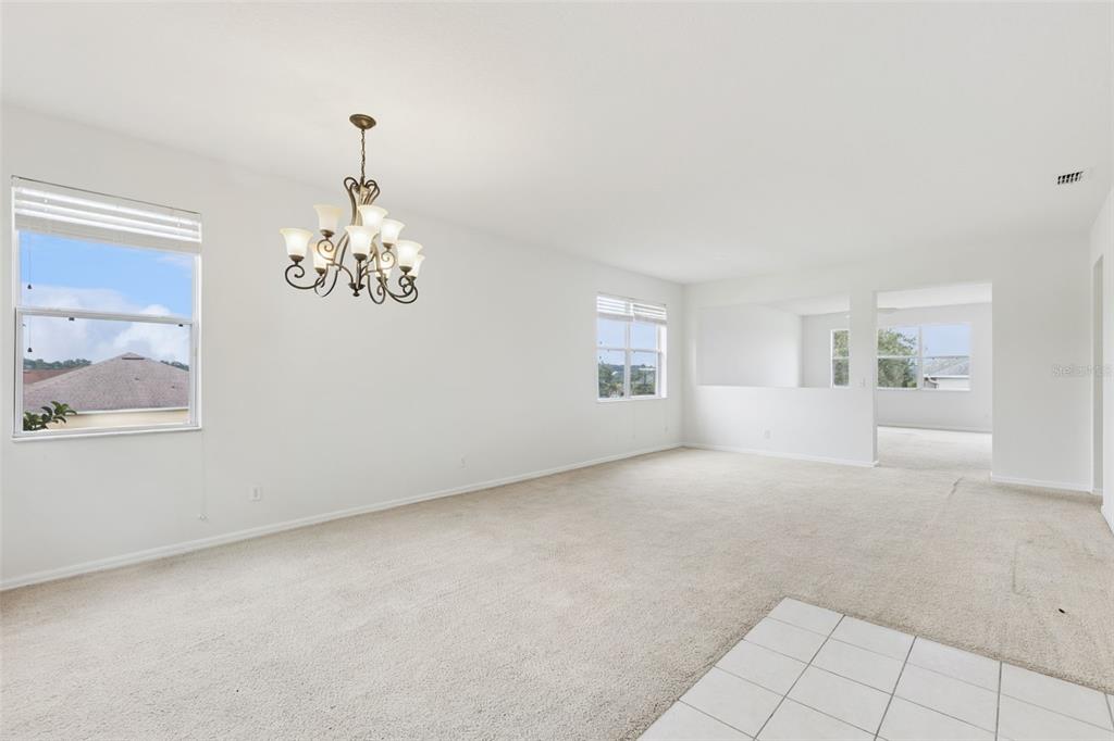 An empty living room features beige carpeting, white walls, a chandelier, and large windows — 780 LAKEVIEW POINTE DRIVE, CLERMONT, FL