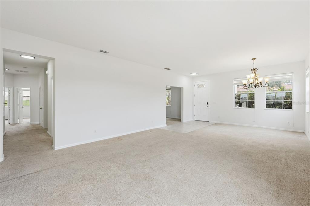 A spacious, carpeted living area features white walls, a dining chandelier, and a front entryway — 780 LAKEVIEW POINTE DRIVE, CLERMONT, FL