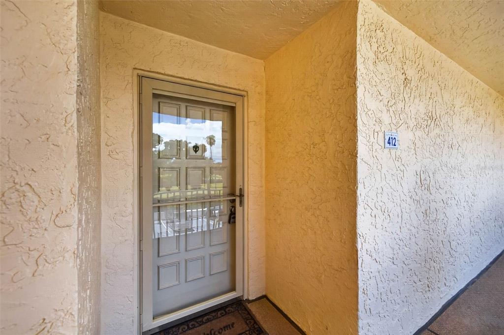 A beige stucco exterior wall features a white storm door and the number 412 — 5541 PUERTA DEL SOL BOULEVARD S UNIT 412, ST PETERSBURG, FL