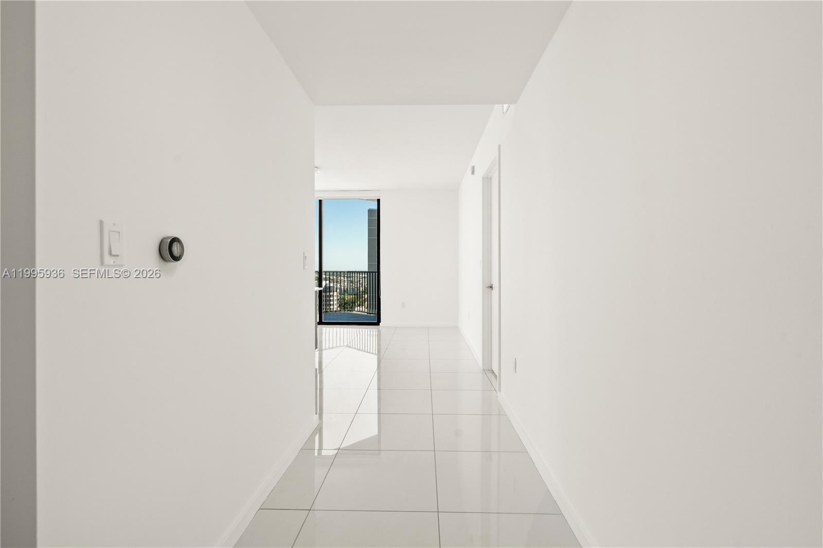 A bright hallway with white walls and glossy tile flooring leads toward a balcony door — 5300 NW 85th St # 1511, Doral FL 33166, DORAL, FL