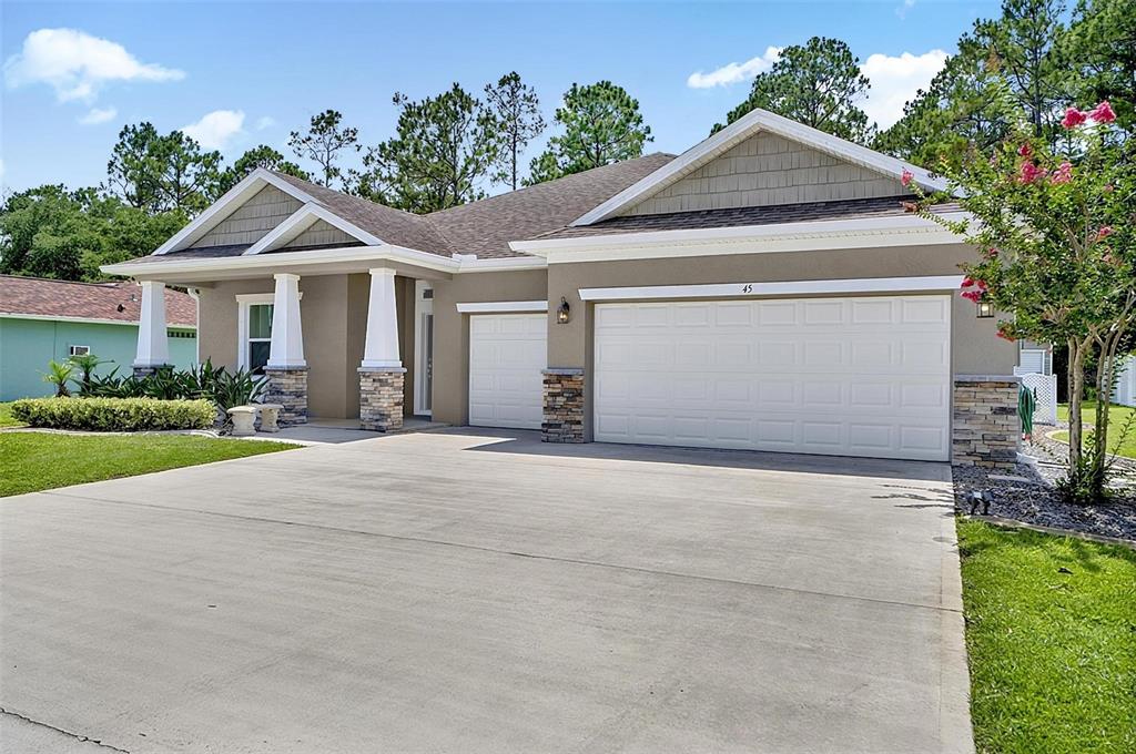 A single-story house with a beige exterior, stone accents, and a three-car garage — 45 ZONAL GERANIUM TRAIL, PALM COAST, FL