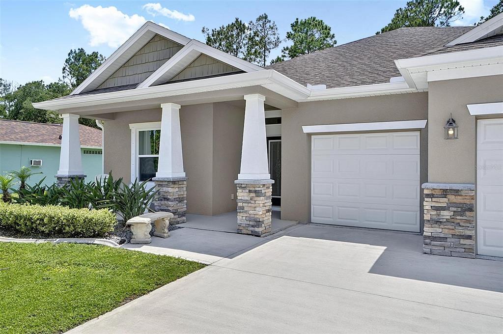A beige house exterior features a stone-accented porch with white columns and a garage — 45 ZONAL GERANIUM TRAIL, PALM COAST, FL