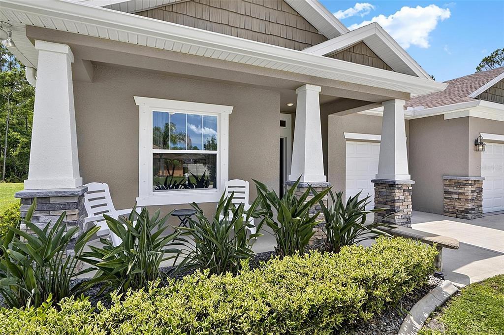 A front porch with white columns, stone bases, and two chairs sits before a house — 45 ZONAL GERANIUM TRAIL, PALM COAST, FL