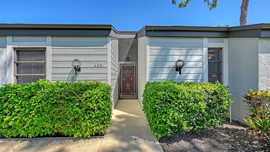A walkway leads to the front entrance of a house with light-colored siding and hedges — 4391 WOODMANS CHART UNIT 155, SARASOTA, FL
