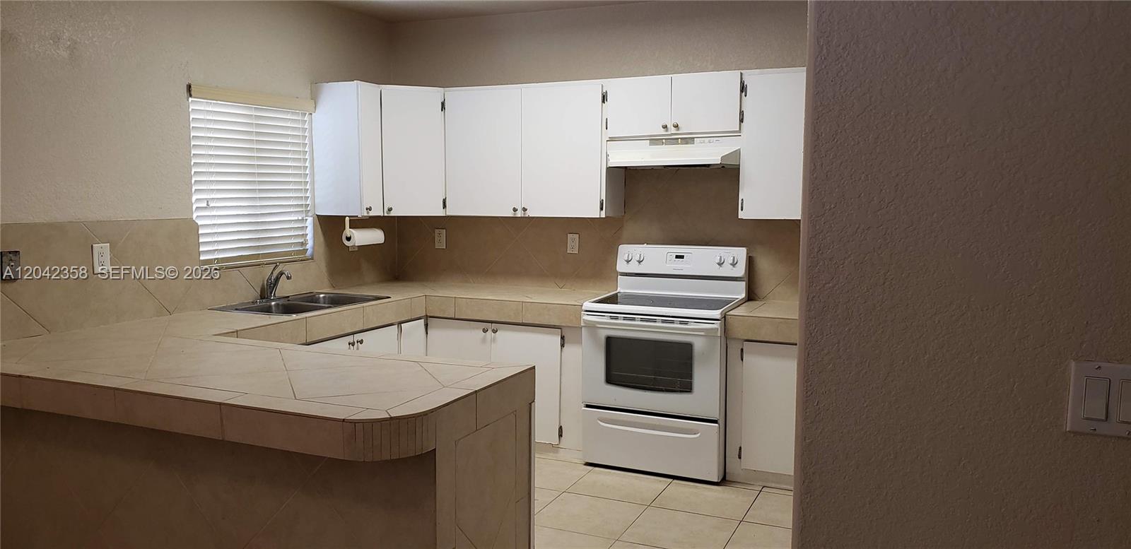 A kitchen features white cabinets, tiled countertops, a white stove, and a double sink — 138 NW 31st St # 138, Miami FL 33127, MIAMI, FL