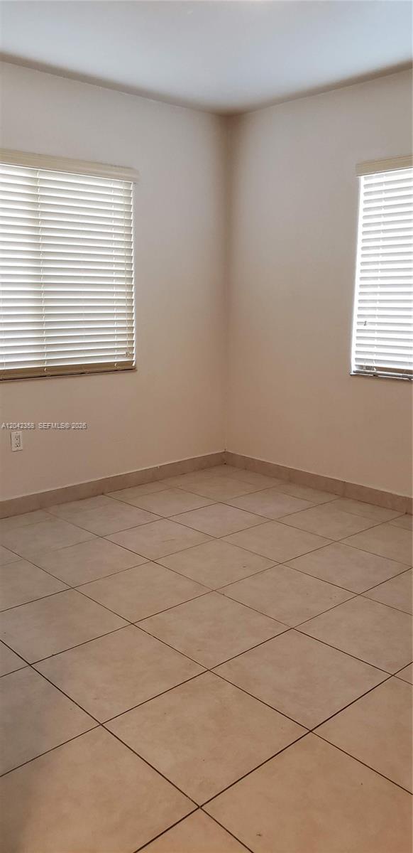 An empty room features beige tile flooring, white walls, and two windows with closed blinds — 138 NW 31st St # 138, Miami FL 33127, MIAMI, FL