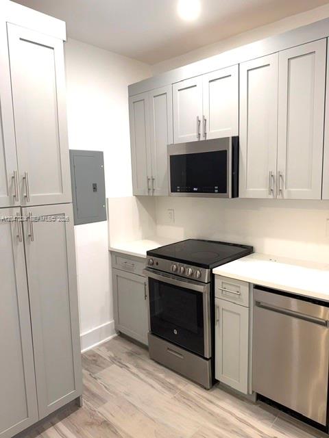 A kitchen features light gray cabinets, stainless steel appliances, and wood-look tile flooring — 1553 Jefferson Ave # 1, Miami Beach FL 33139, MIAMI BEACH, FL