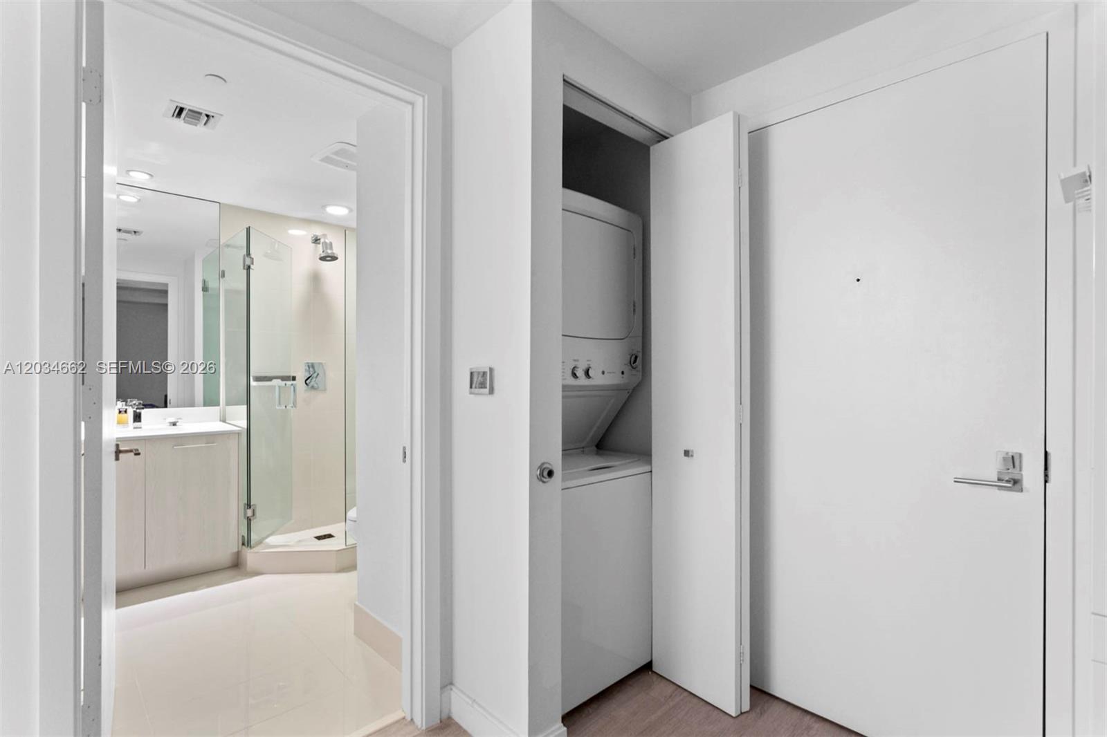 A white laundry closet with a stacked washer and dryer sits beside a bathroom entrance — 55 SW 9th St # 1105, Miami FL 33130, MIAMI, FL