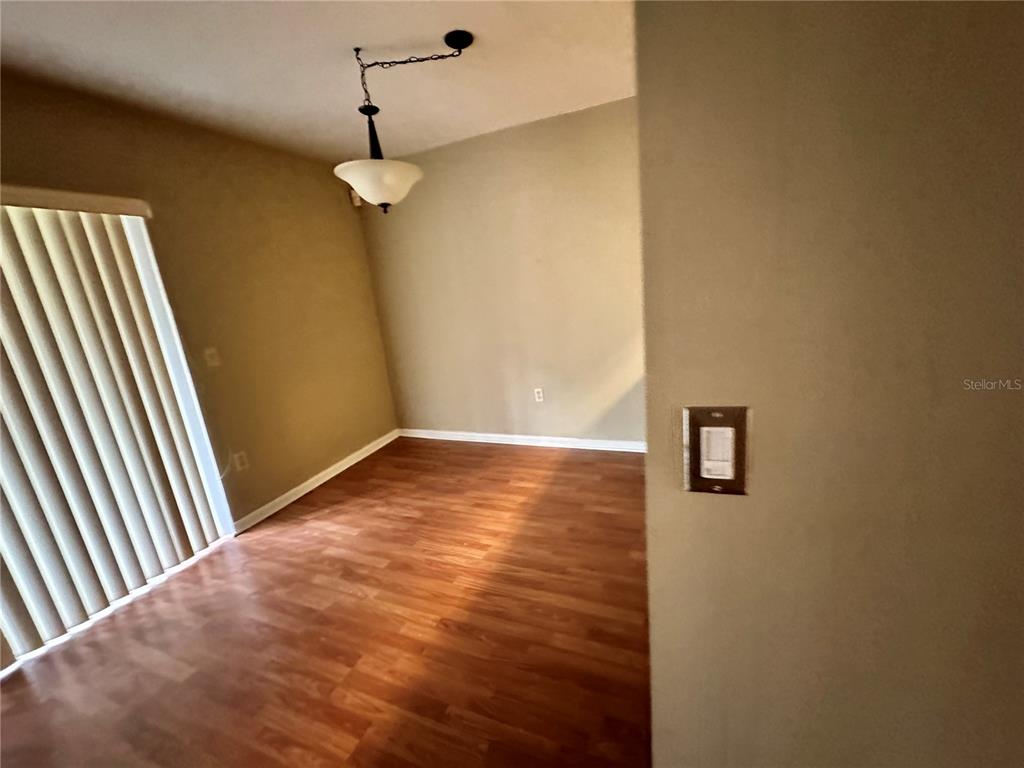 An empty room features wood-look flooring, a hanging light fixture, and a sliding glass door — 2735 SW 35TH PLACE UNIT 2001, GAINESVILLE, FL