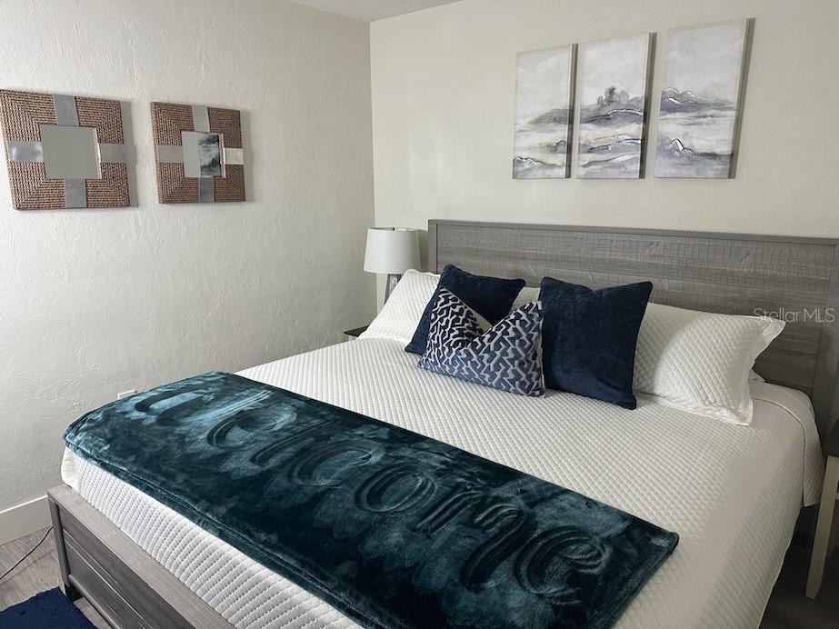 A bedroom features a bed with a teal throw blanket, navy pillows, and wall art — 1912 MORRILL UNIT 1920, SARASOTA, FL