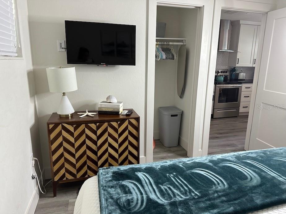 A bedroom with a patterned dresser, wall-mounted television, and an open closet leading to a kitchen — 1912 MORRILL UNIT 1920, SARASOTA, FL