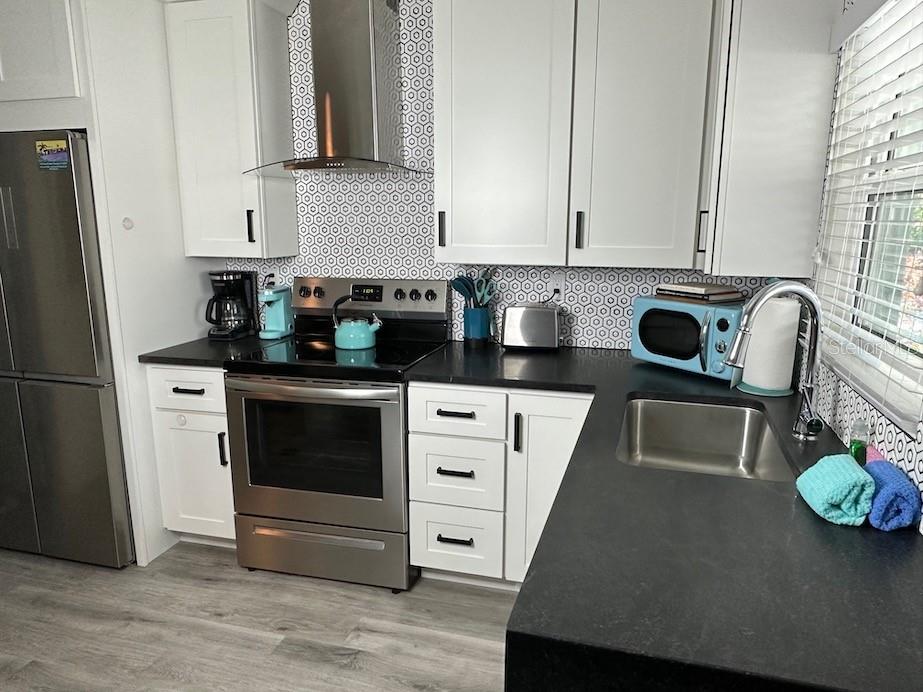 A kitchen features white cabinets, black countertops, stainless steel appliances, and a geometric patterned backsplash — 1912 MORRILL UNIT 1920, SARASOTA, FL