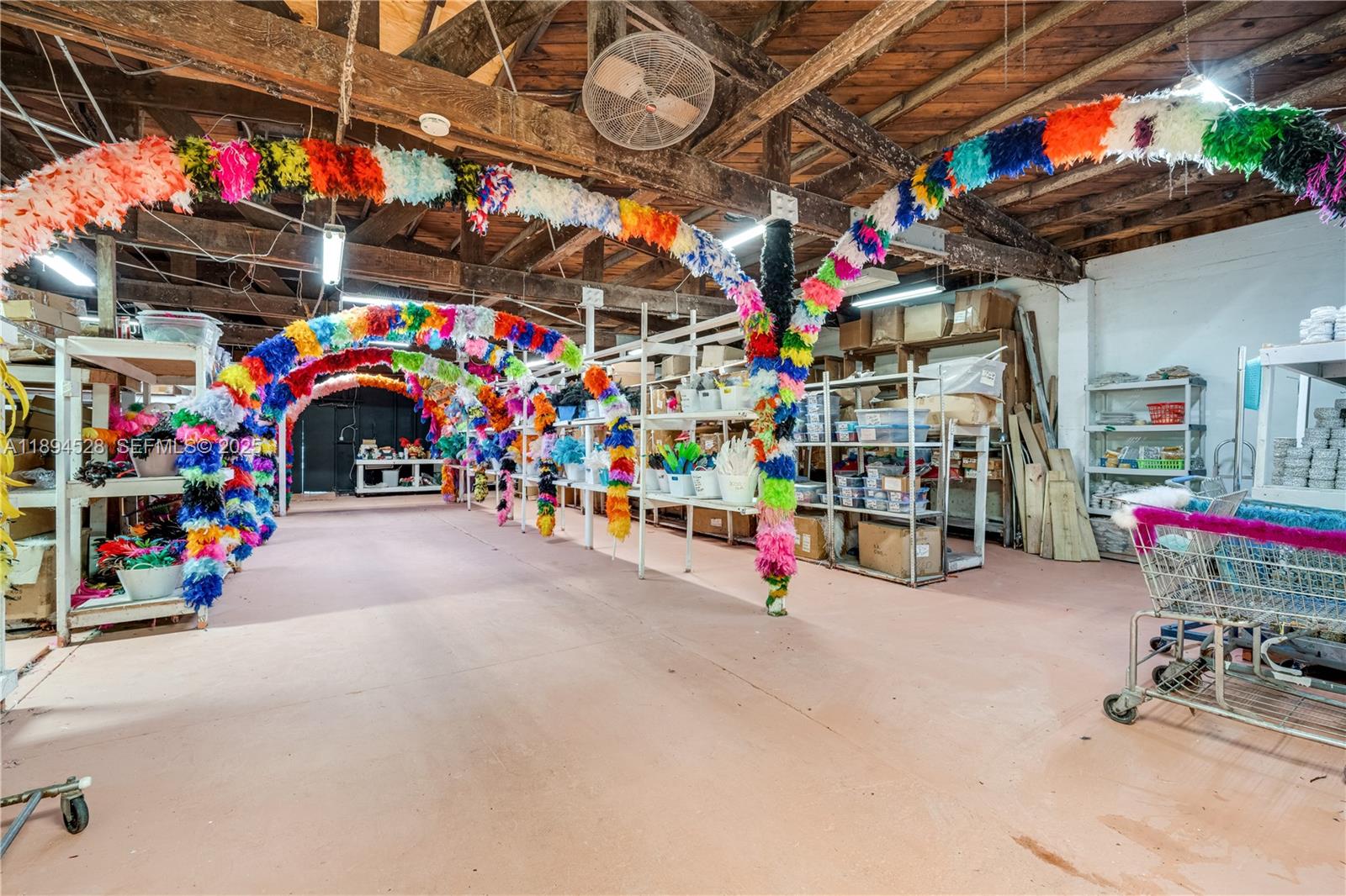 A warehouse space features exposed wooden beams, concrete floors, and colorful feather boa arches — 1121 NW 29th St, Miami FL 33127, MIAMI, FL