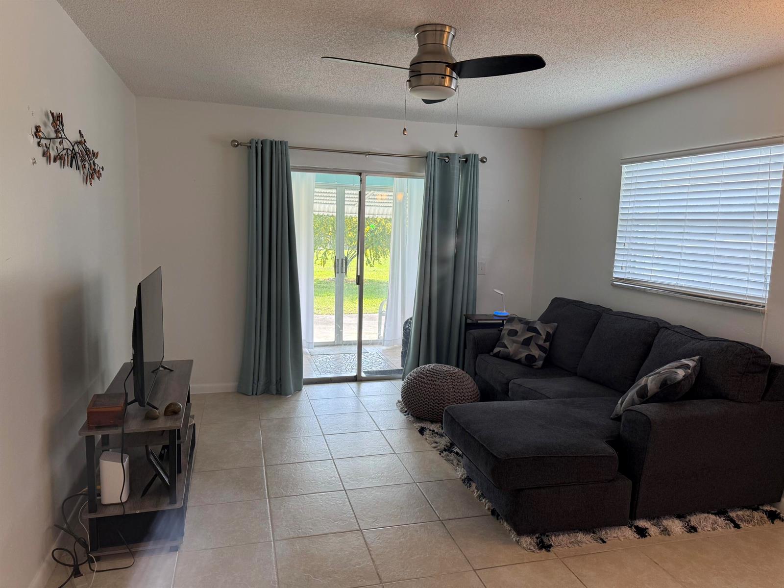 A living room features a dark gray sectional sofa, a television stand, and sliding glass doors — 300 SW Golfview Terrace # 152, Boynton Beach FL 33426, BOYNTON BEACH, FL