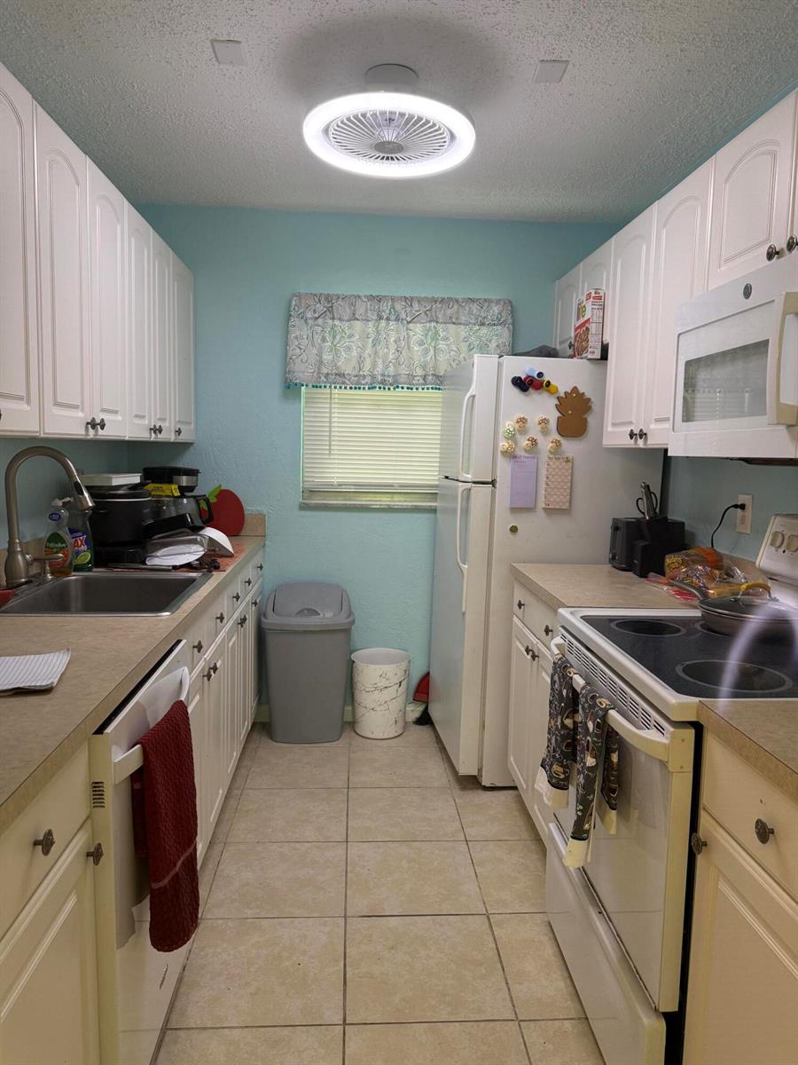 A galley kitchen features white cabinets, light countertops, a tiled floor, and a ceiling fan light — 300 SW Golfview Terrace # 152, Boynton Beach FL 33426, BOYNTON BEACH, FL