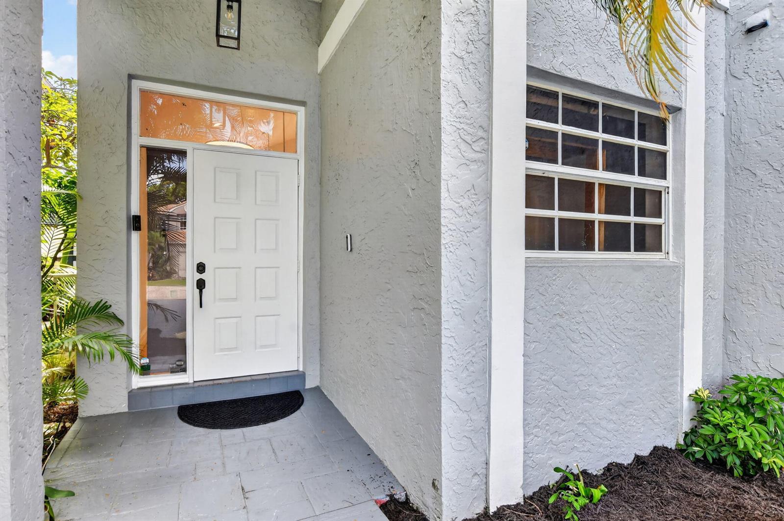 A white front door with a sidelight and transom window sits on a gray porch — 23338 La Vida Way, Boca Raton FL 33433, BOCA RATON, FL