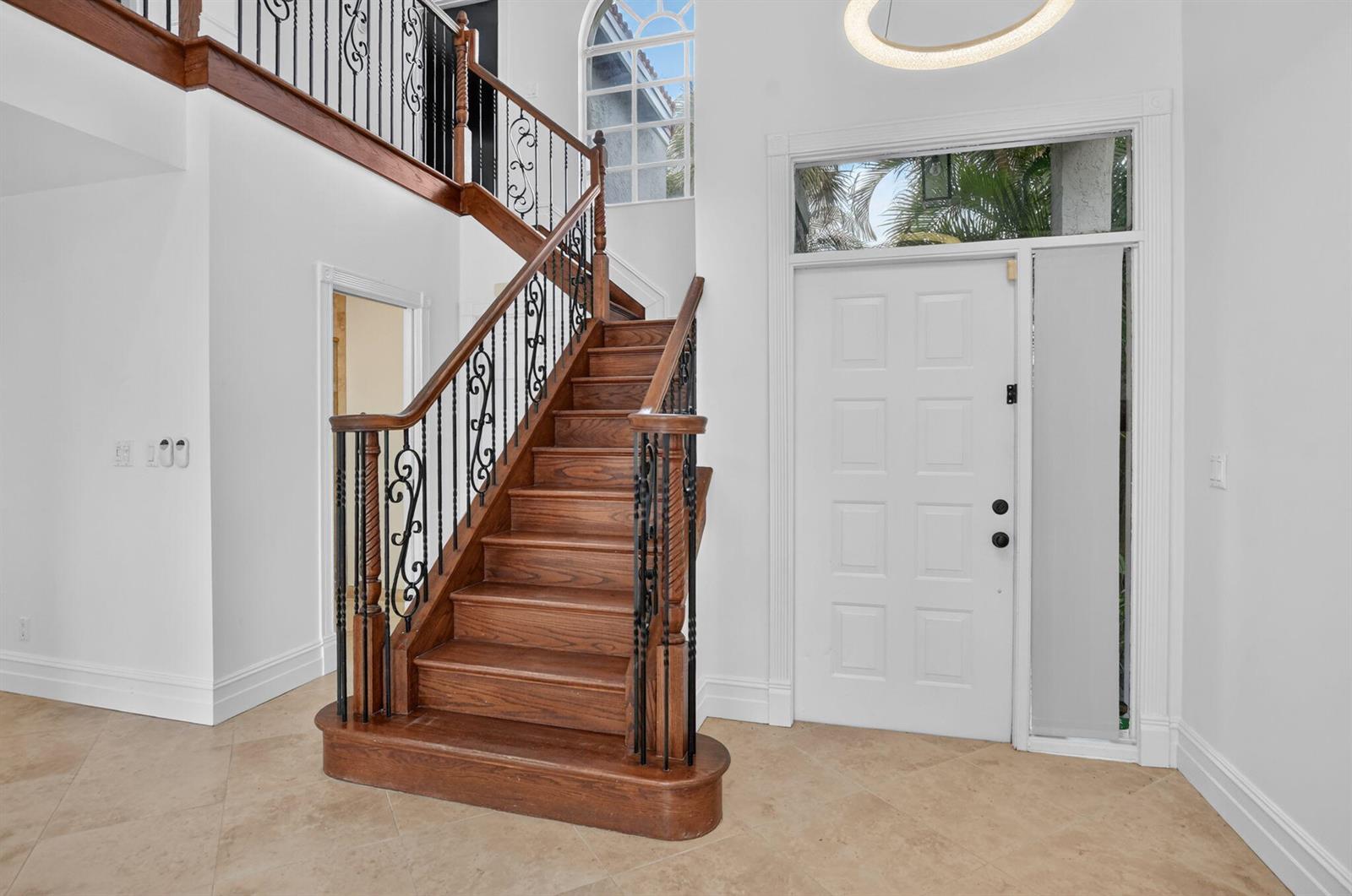 A foyer features a wooden staircase with black iron railings and a white front door — 23338 La Vida Way, Boca Raton FL 33433, BOCA RATON, FL