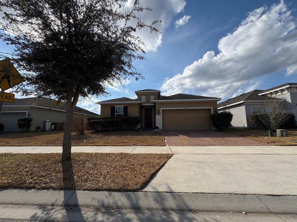 A single-story suburban house with a tan exterior, brick driveway, and a front-facing garage — 4813 MARCOS CIRCLE, KISSIMMEE, FL
