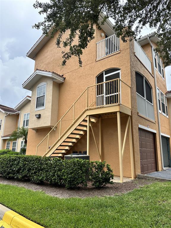 Exterior view of a multi-story tan stucco building with an outdoor staircase and garage — 12031 VILLANOVA DRIVE UNIT 110, ORLANDO, FL