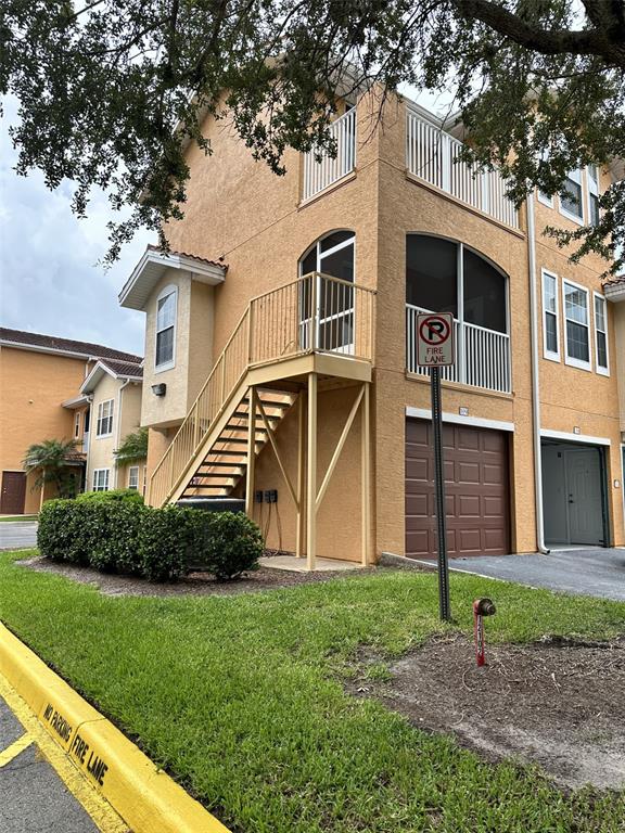 Exterior view of a multi-story tan stucco building with an outdoor staircase and garage — 12031 VILLANOVA DRIVE UNIT 110, ORLANDO, FL