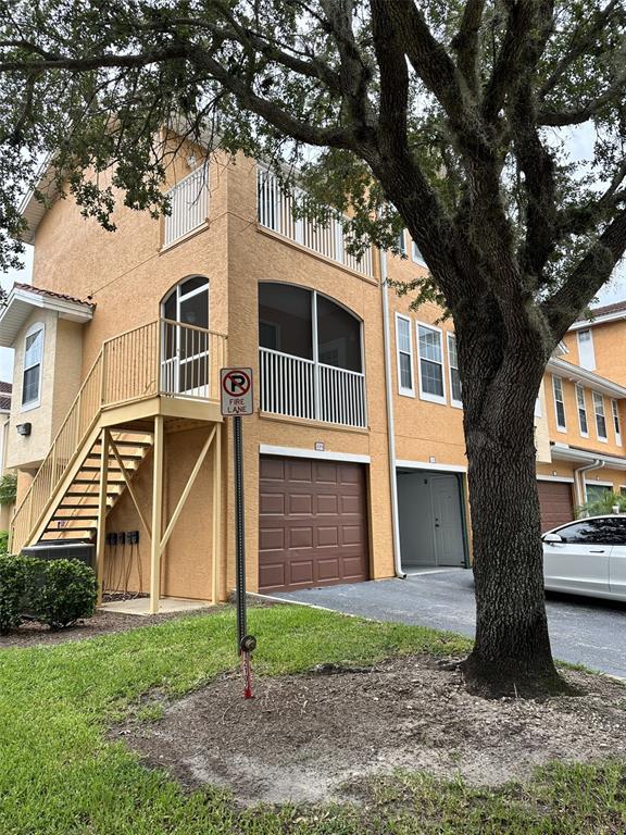 Exterior view of a multi-story tan stucco building with a staircase, garage, and large tree — 12031 VILLANOVA DRIVE UNIT 110, ORLANDO, FL