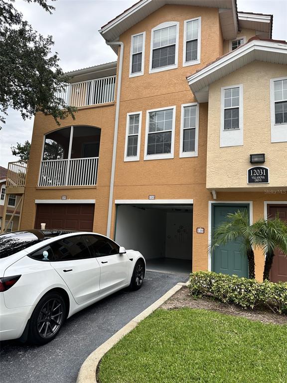 A white Tesla is parked in front of a three-story tan building with a garage — 12031 VILLANOVA DRIVE UNIT 110, ORLANDO, FL
