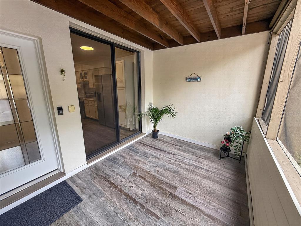 A covered patio features wood-look flooring, a sliding glass door, and a small potted plant — 1111 N BAYSHORE BOULEVARD UNIT E3, CLEARWATER, FL