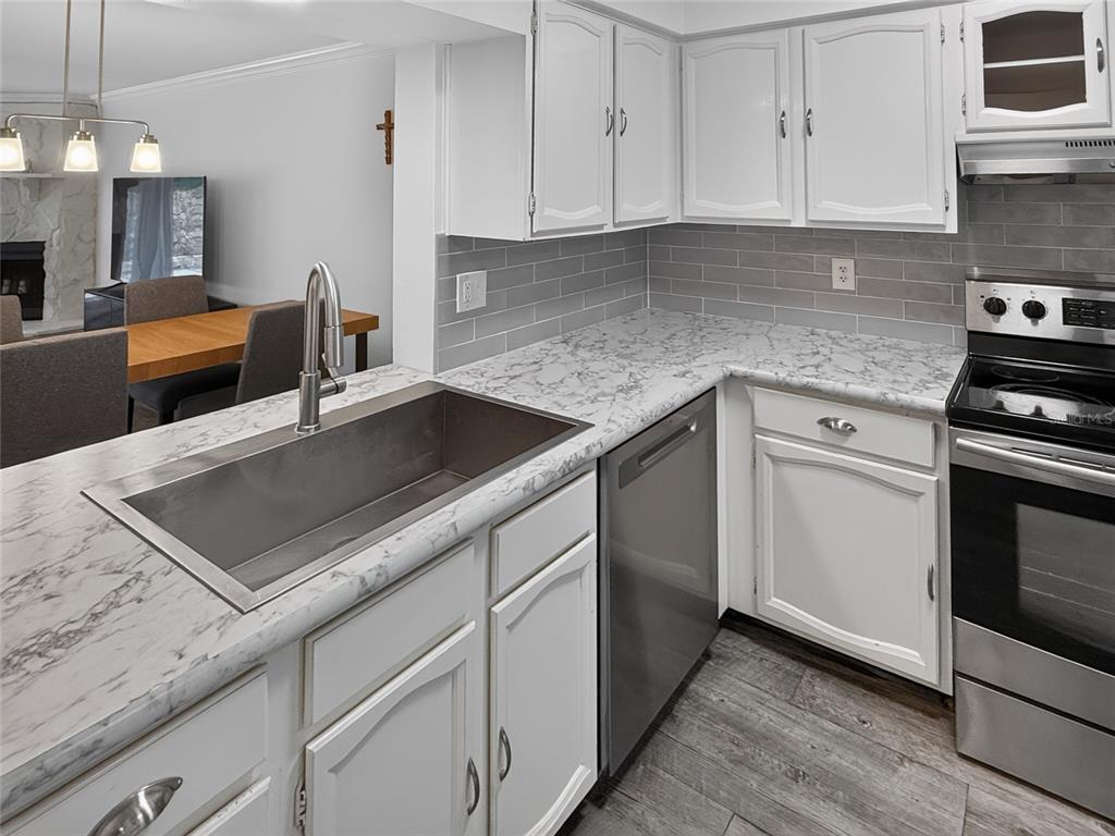 A kitchen features white cabinets, marble-look countertops, a stainless steel sink, and gray subway tile — 1111 N BAYSHORE BOULEVARD UNIT E3, CLEARWATER, FL