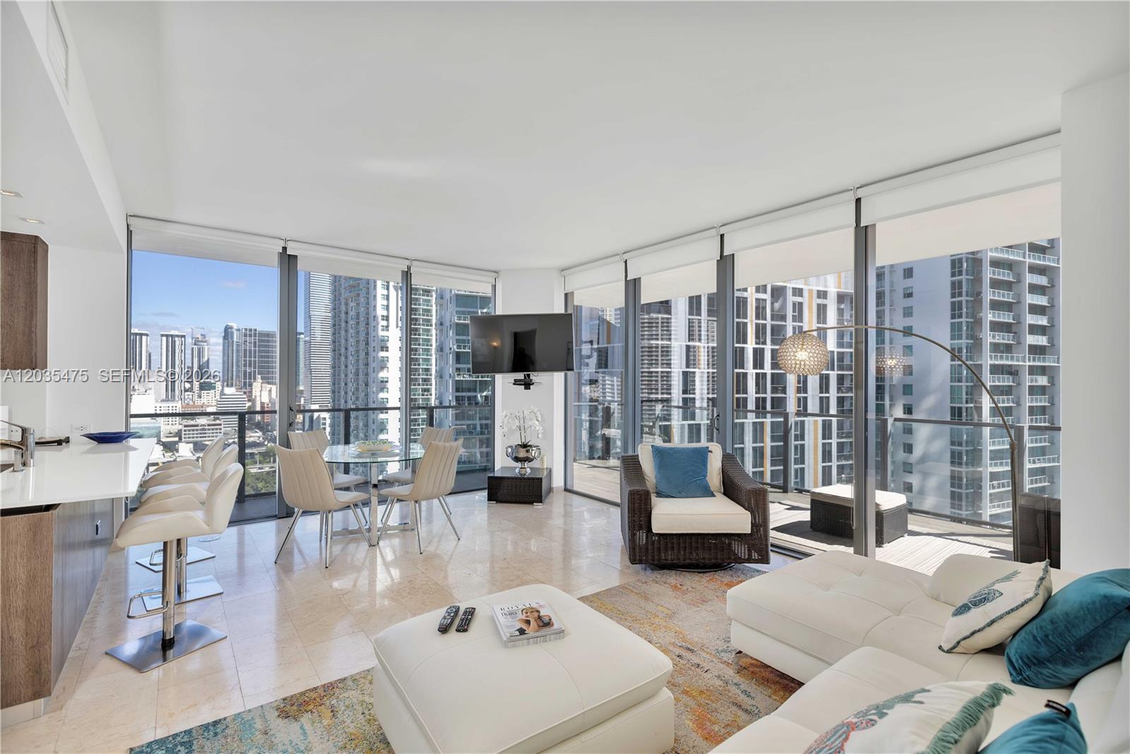 A modern living room with floor-to-ceiling windows, white tile floors, and a city skyline view — 68 SE 6th St # 1611, Miami FL 33131, MIAMI, FL