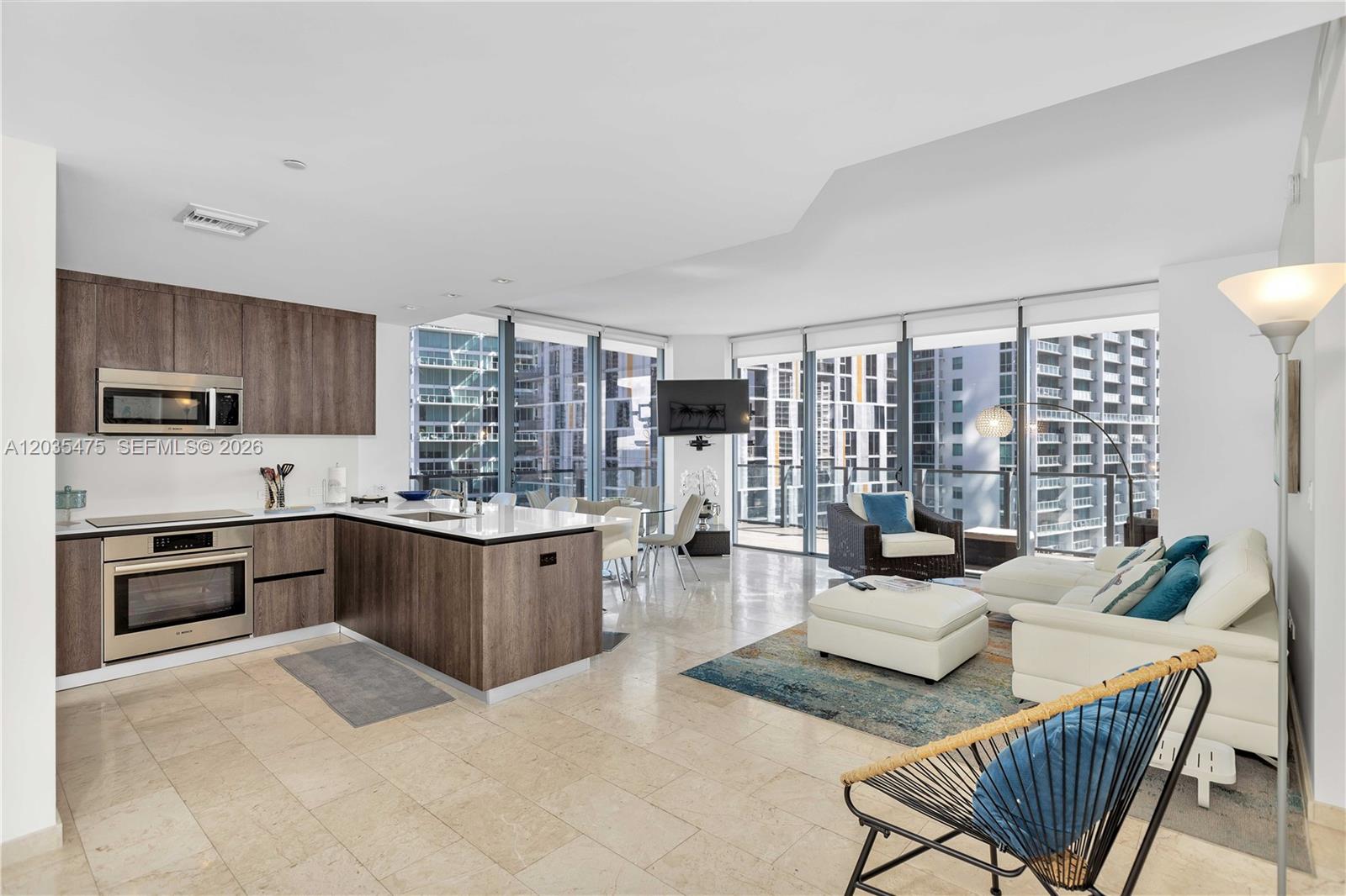 A modern open-concept kitchen and living area features wood cabinetry, tile floors, and floor-to-ceiling windows — 68 SE 6th St # 1611, Miami FL 33131, MIAMI, FL